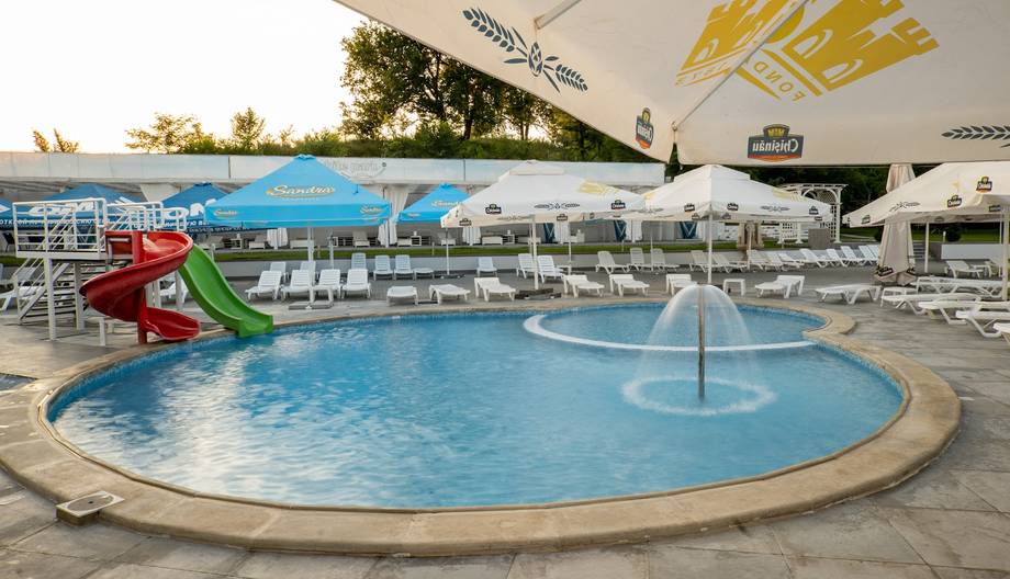 Resort pool area with water slide, fountain, and loungers overlooking grounds