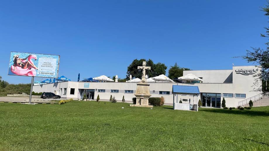 White monastery building with cross and surrounding grounds under clear sky