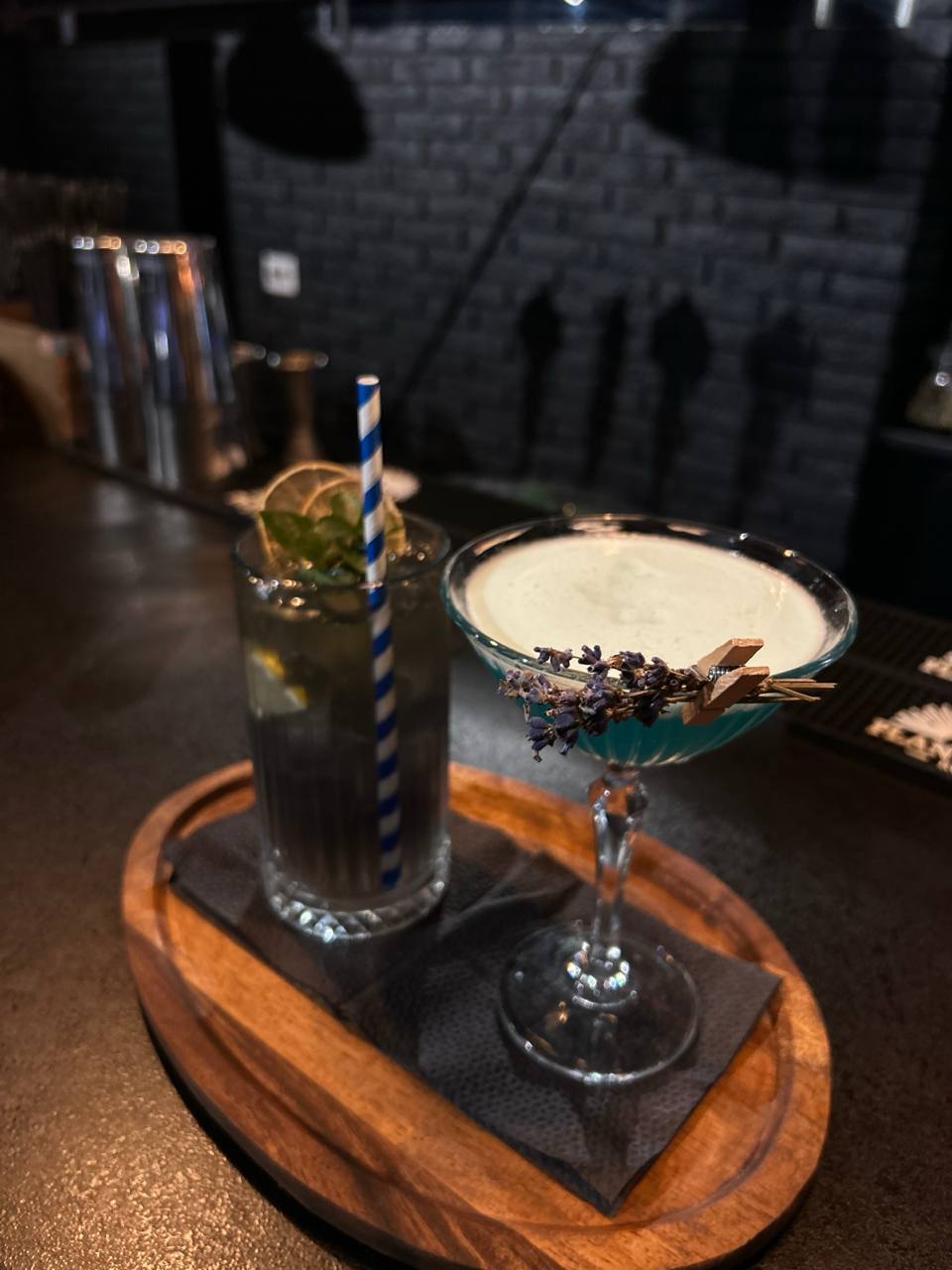 Craft cocktails with lavender garnish and black straw on wooden serving board