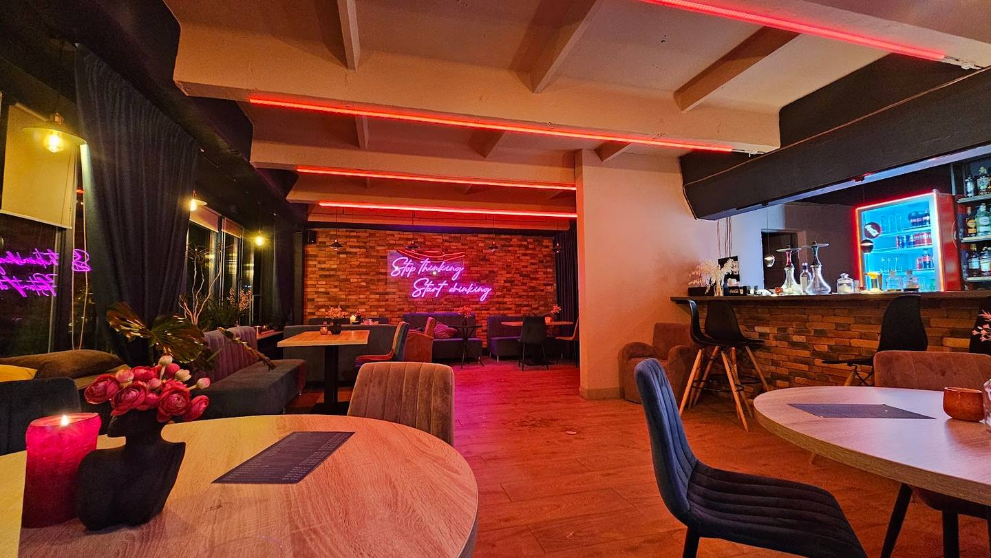 Modern lounge interior with neon signage, dining tables, and ambient lighting