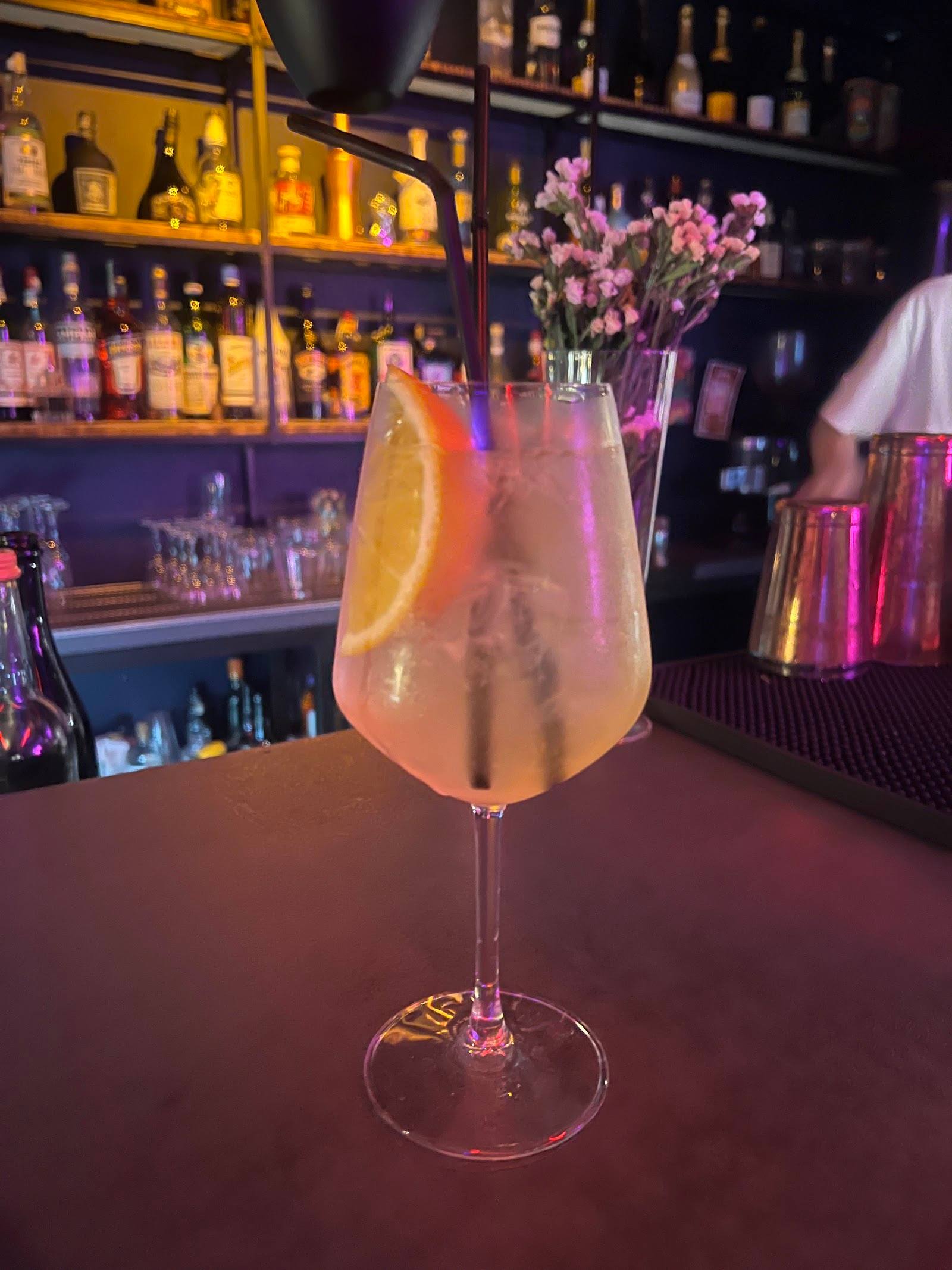 Signature cocktail with lemon garnish and fresh flowers on back bar with illuminated bottle display