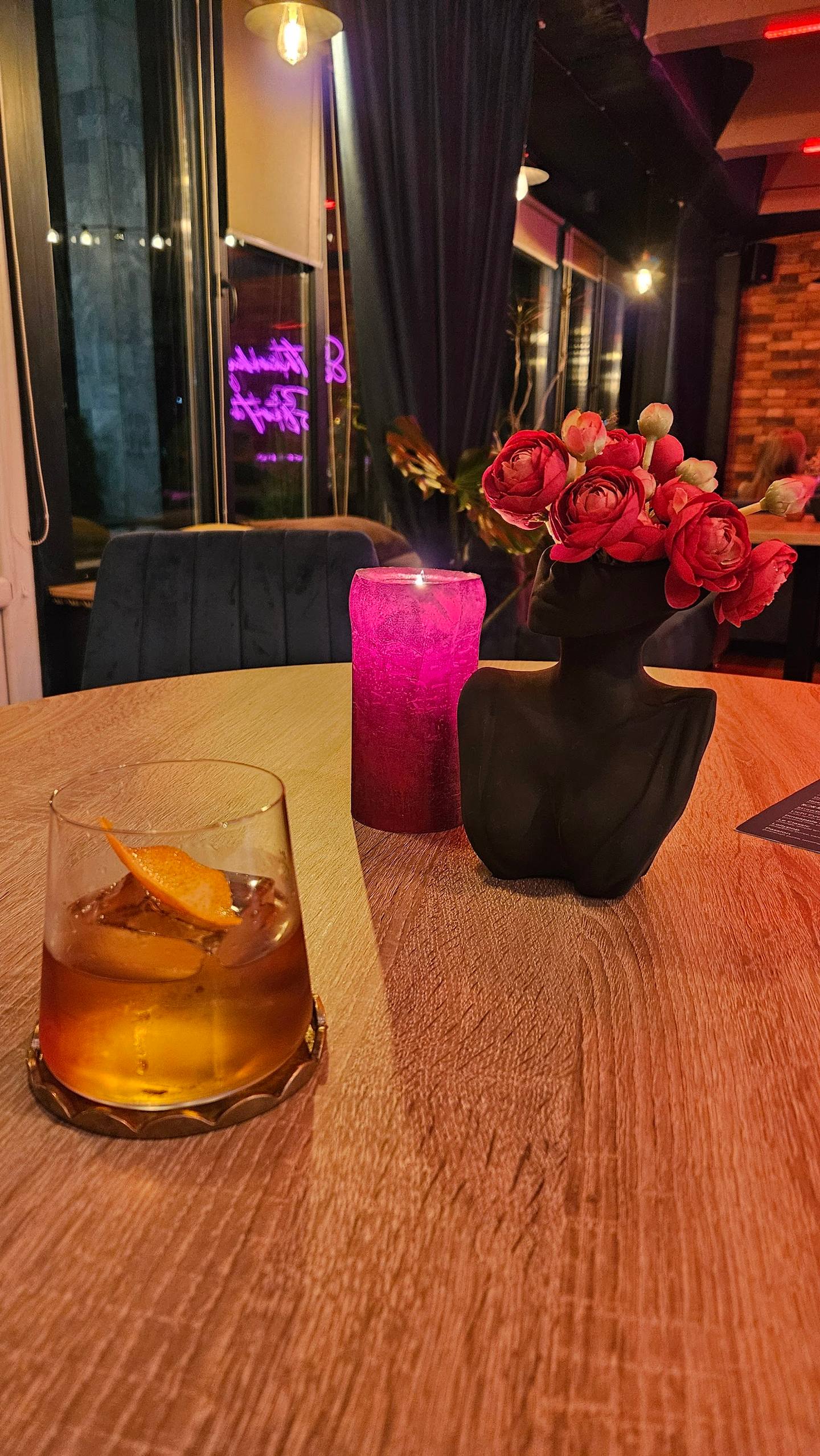 Intimate table setting with cocktail, pink candle, and fresh flowers in modern bar interior