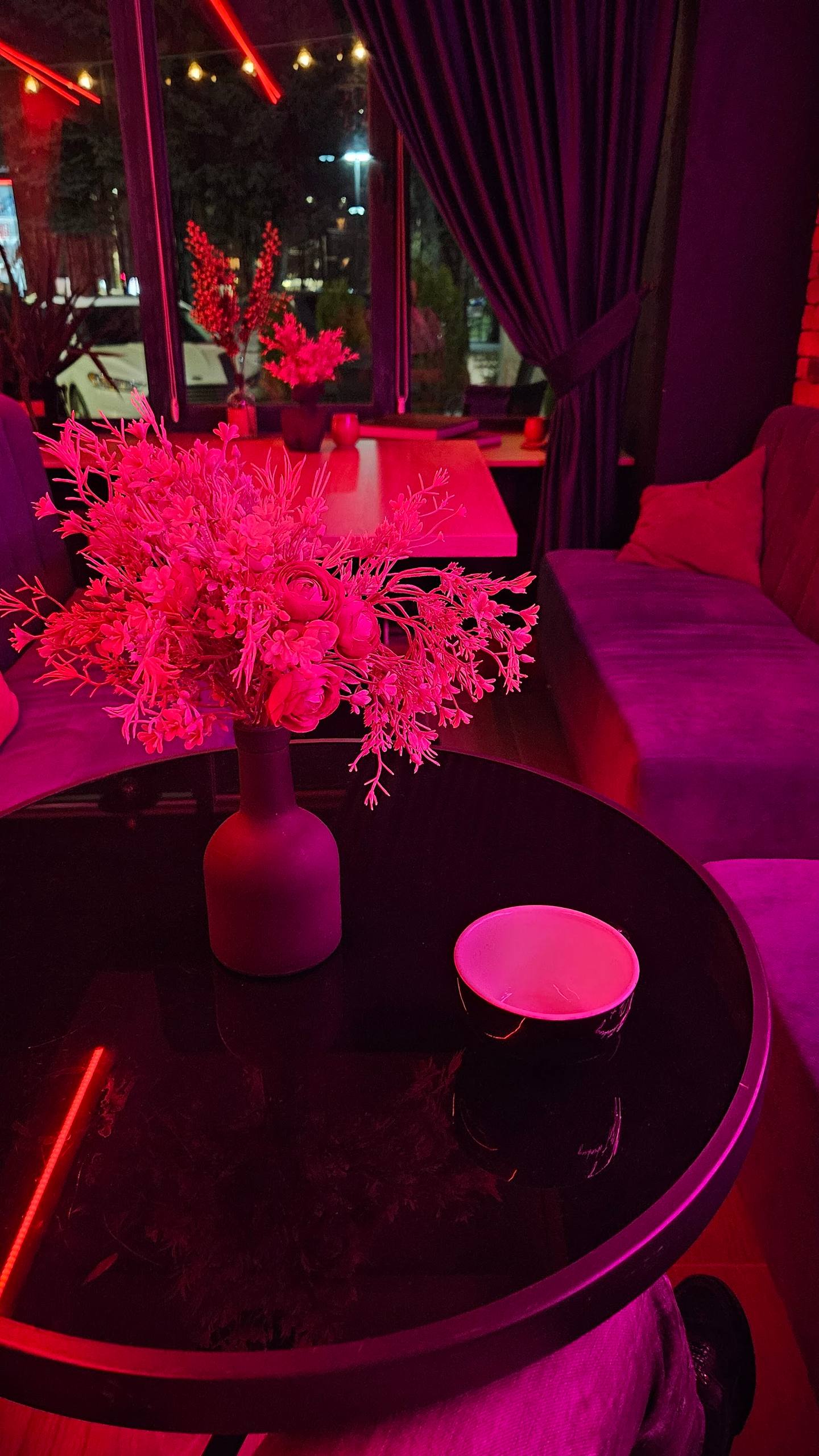 Moody nightclub lounge with neon pink lighting and city view through windows