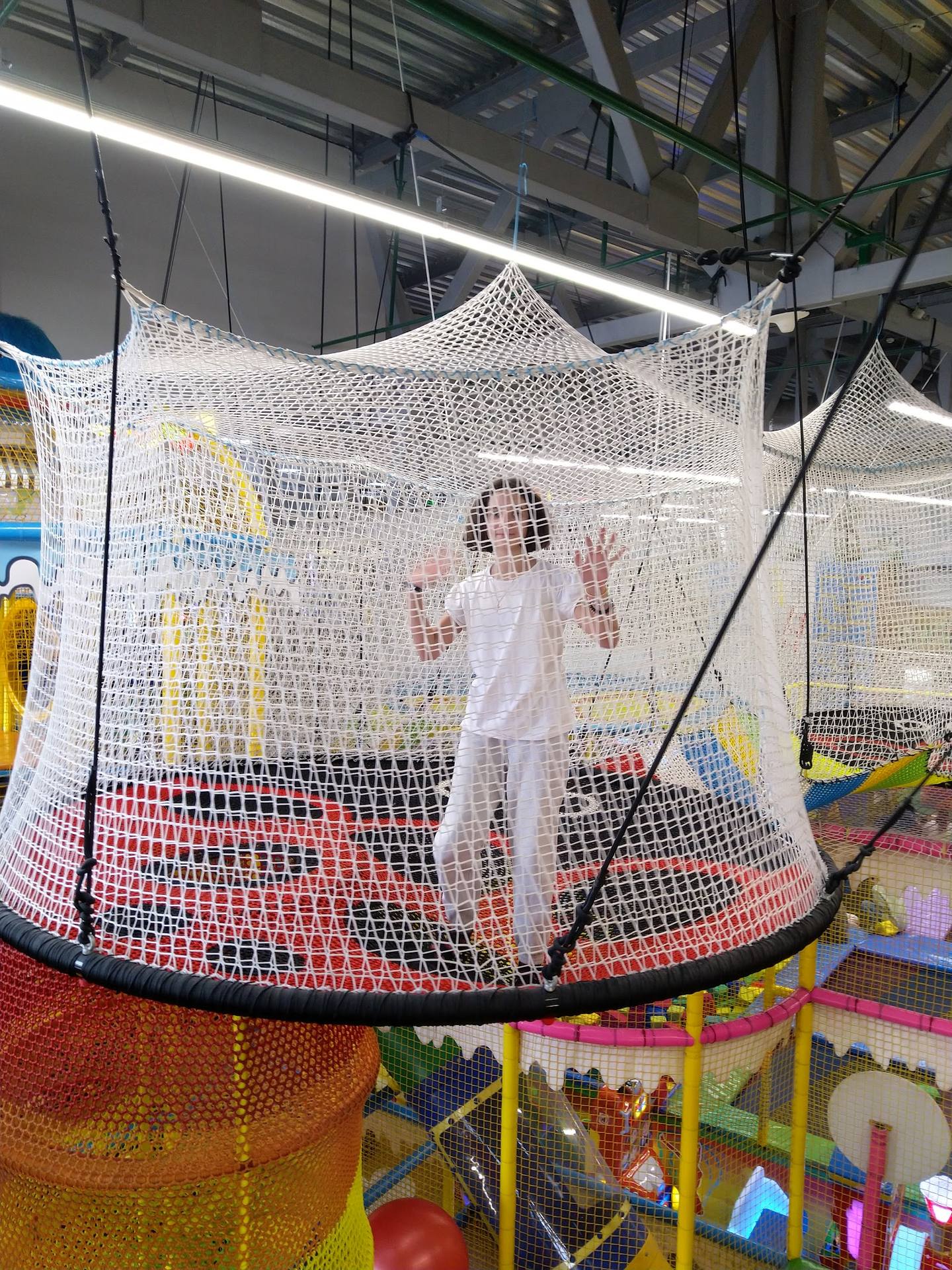 Child playing in indoor trampoline net arena with colorful foam pit