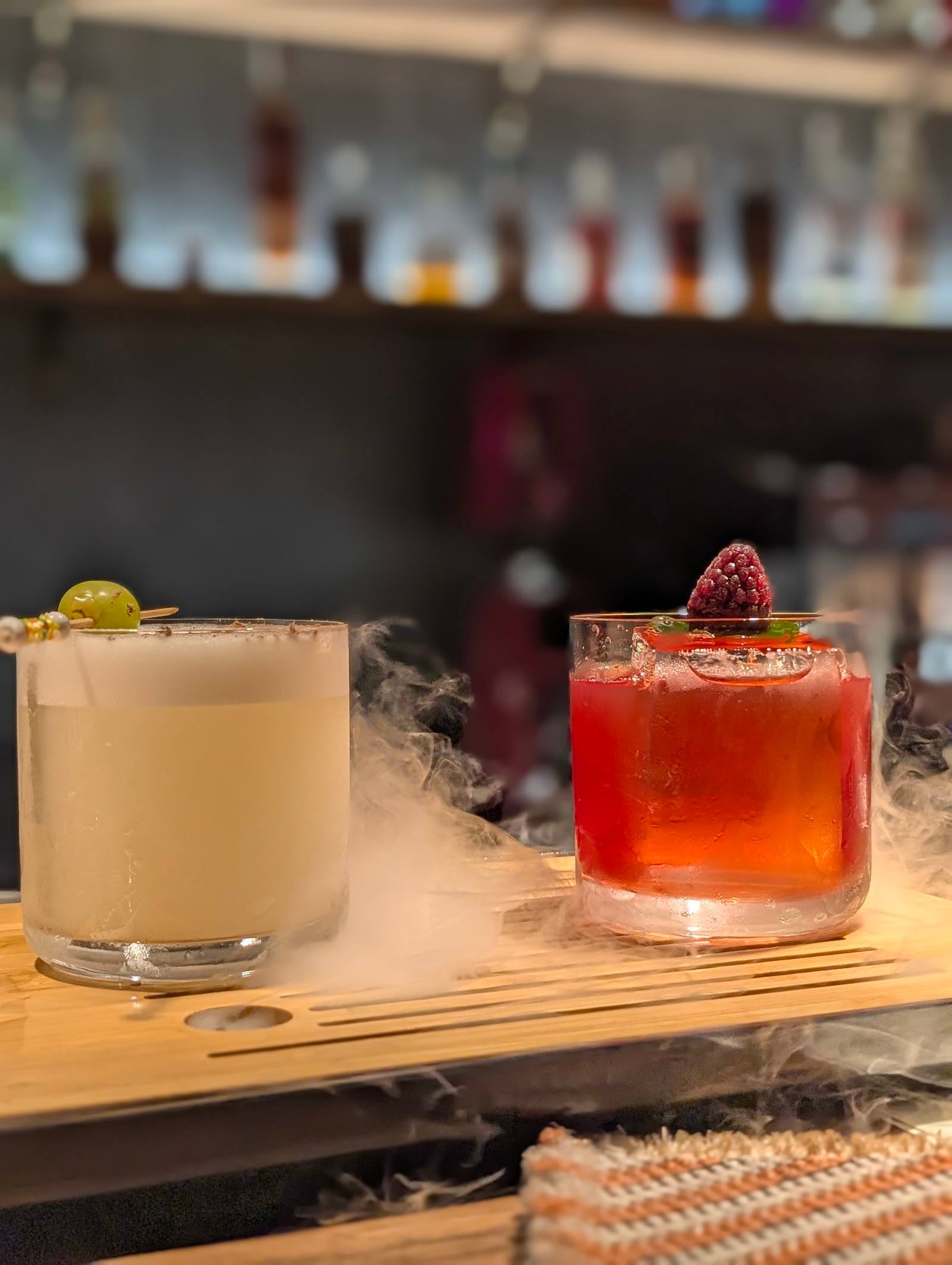 Two artisanal cocktails with dramatic dry ice vapor on wooden bar tray