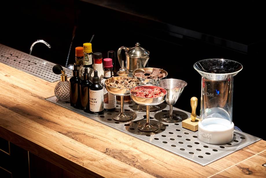 Bar setup with cocktails, bottles, and barware on wooden counter