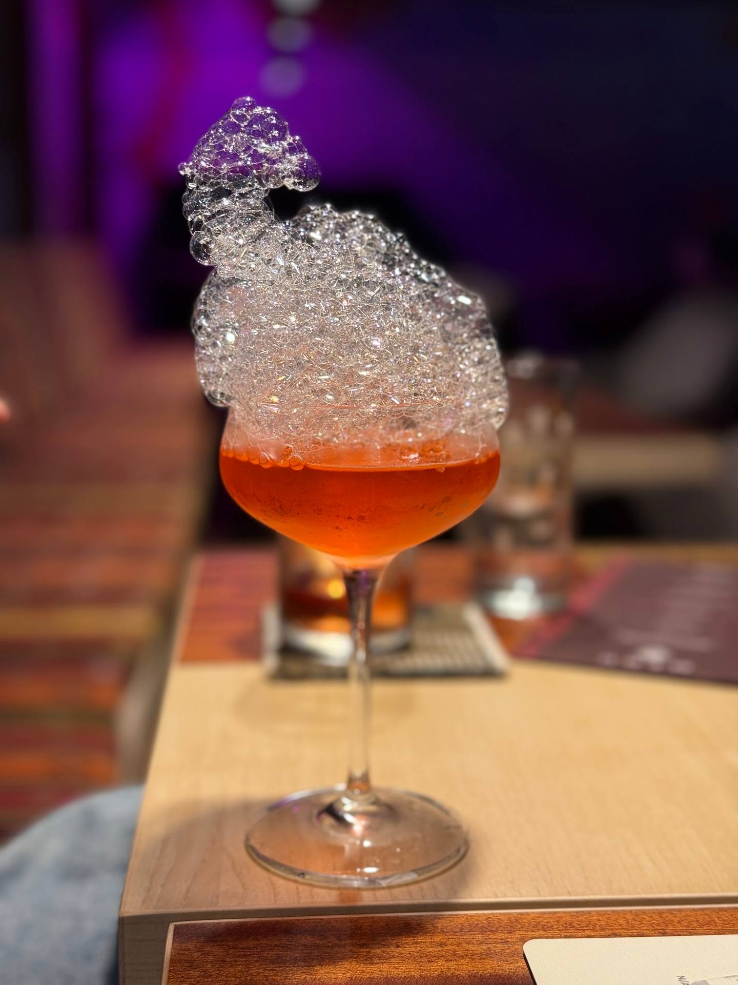 Craft cocktail with crystallized sugar rim and purple ambient lighting