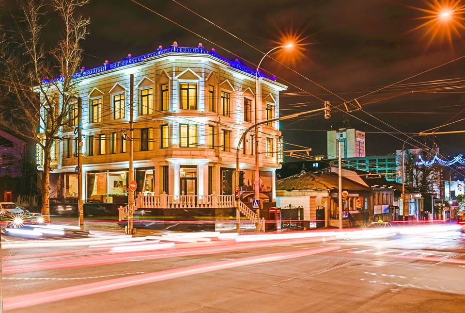 Iconic yellow colonial building with blue-lit roof at night, street-level evening view