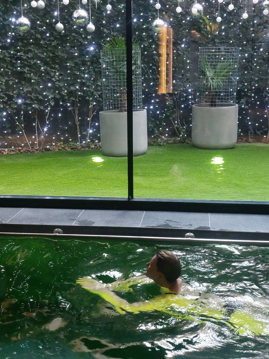 Swimmer in heated indoor pool with decorated garden view beyond glass wall