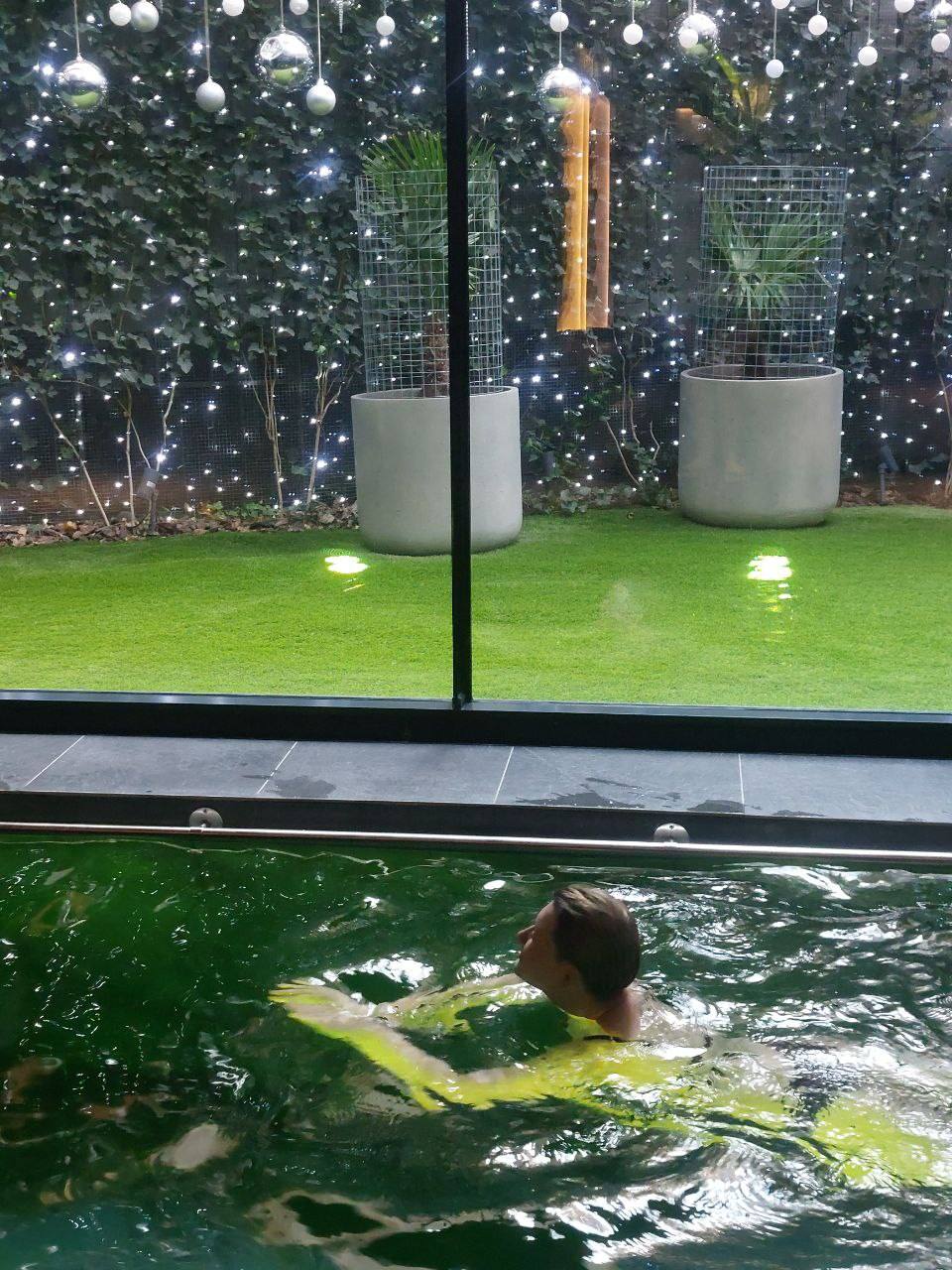 Swimmer in heated indoor pool with decorated garden view beyond glass wall