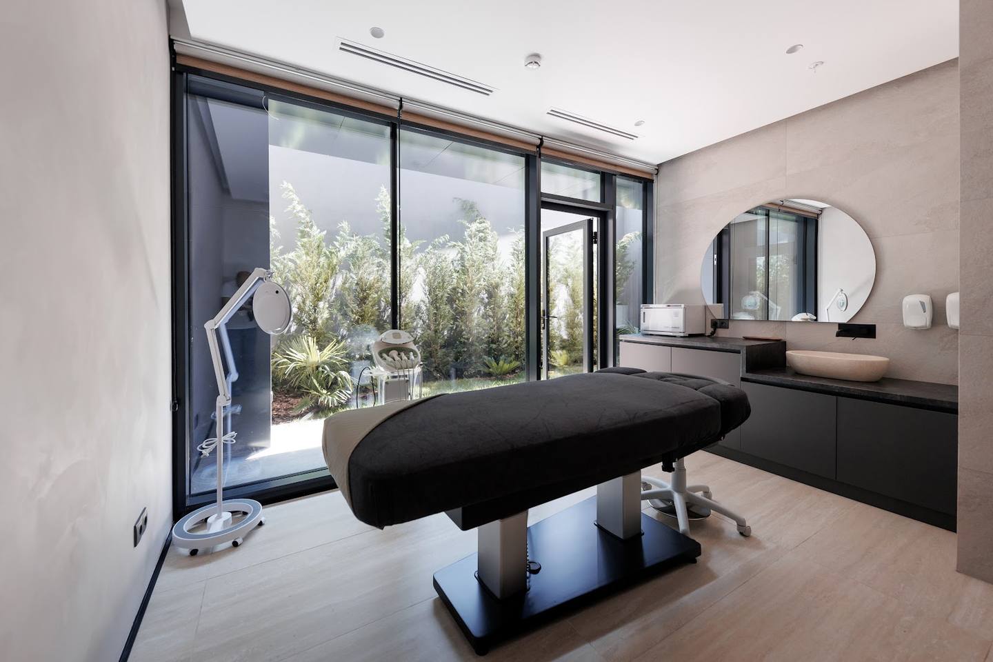 Modern spa treatment room with massage table and scenic garden views through floor-to-ceiling windows