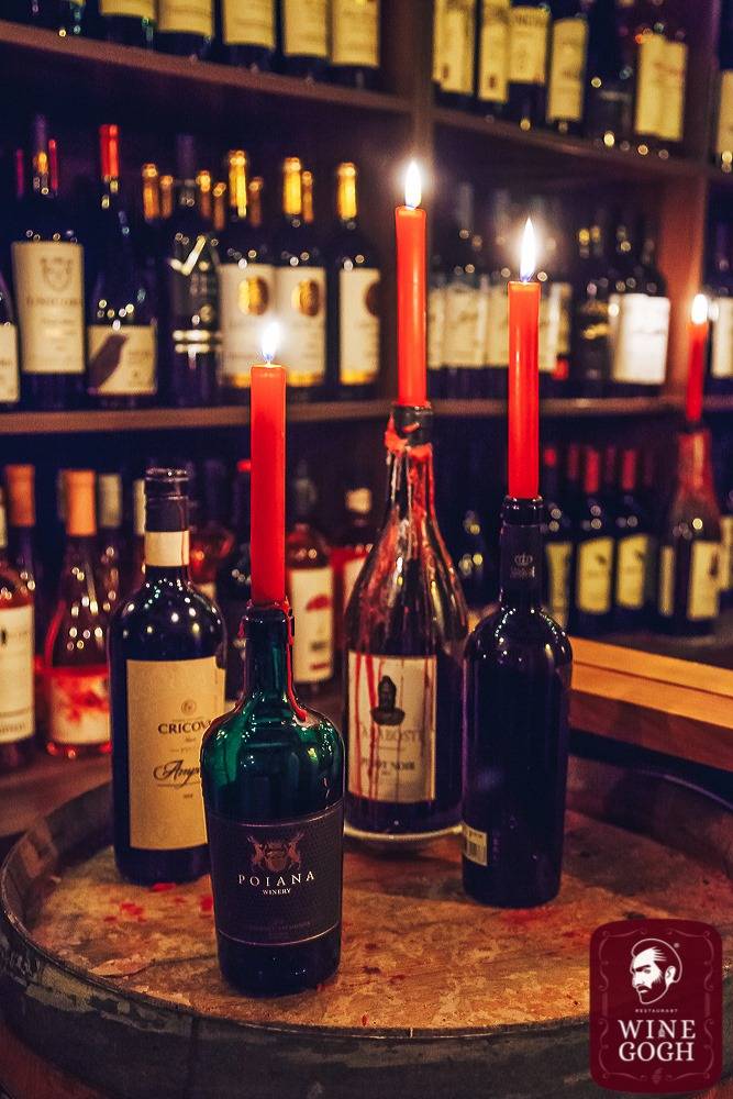 Wine bottles with red candles displayed on table against illuminated bottle wall