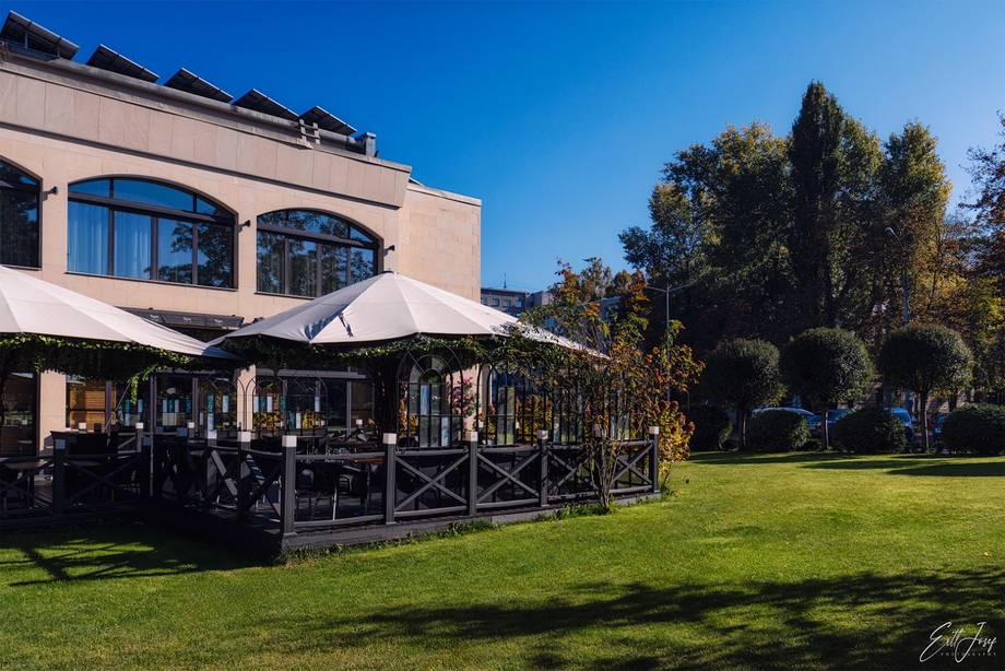 Modern terrace with cream awning overlooking manicured green lawn, rose-colored building and mature trees