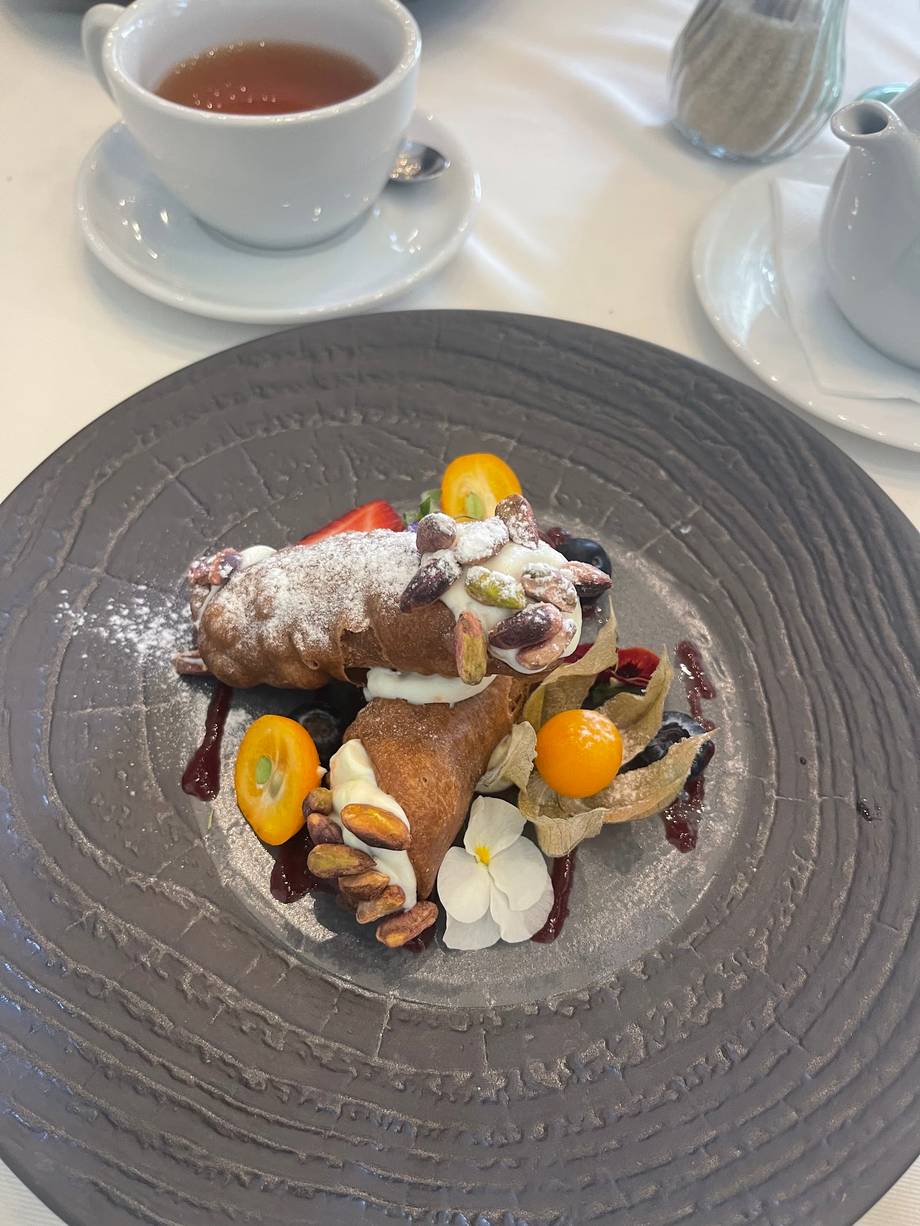 Plated dessert with pastries, edible flowers, and powdered sugar on dark plate with tea service