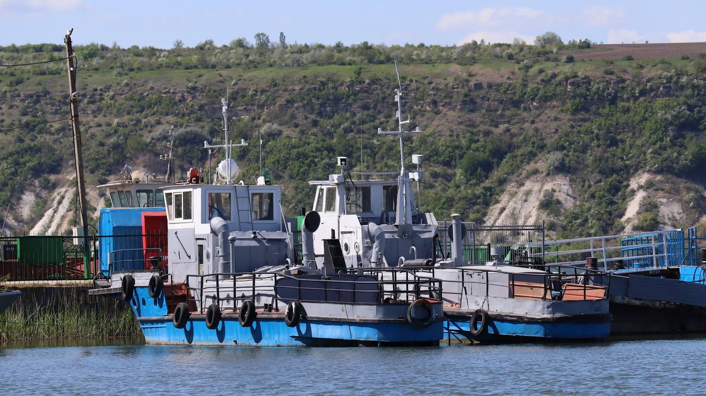 River port with industrial vessels and docked boats on scenic waterway with forested banks