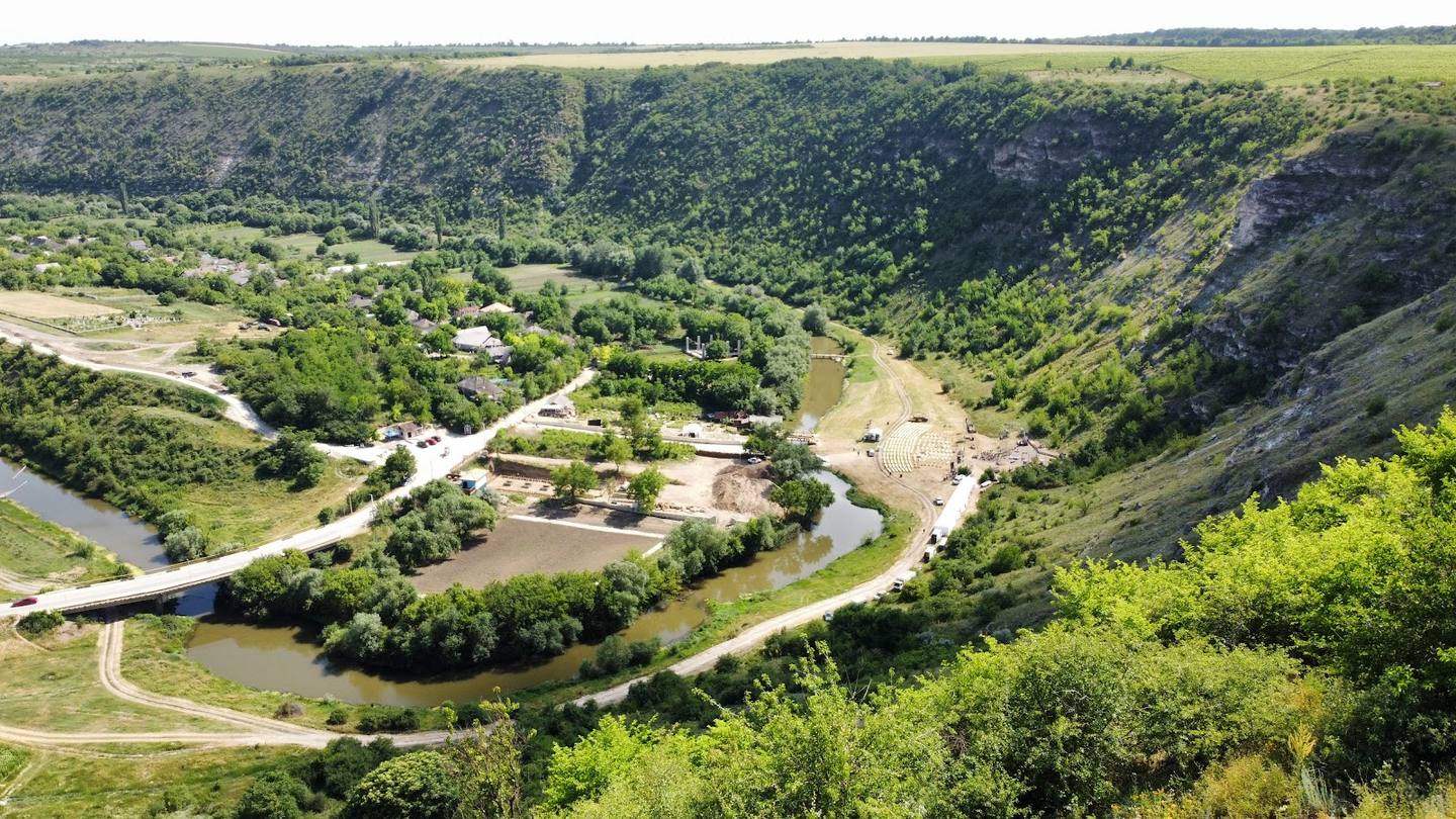 Aerial view of meandering river valley with venue buildings nestled among green hills and forests
