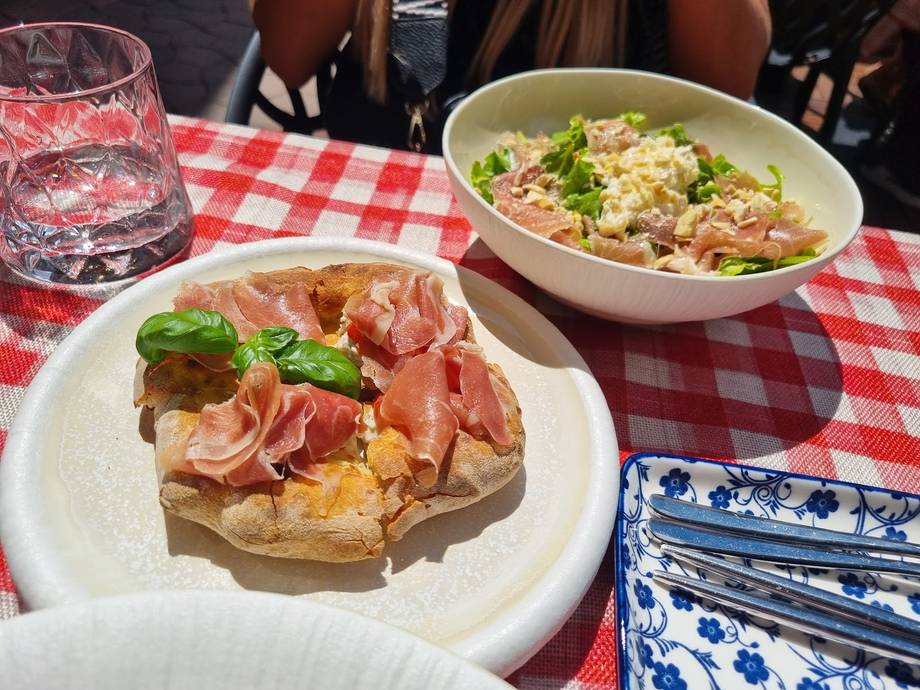 Plated dishes with prosciutto and fresh salad on red checkered outdoor tablecloth