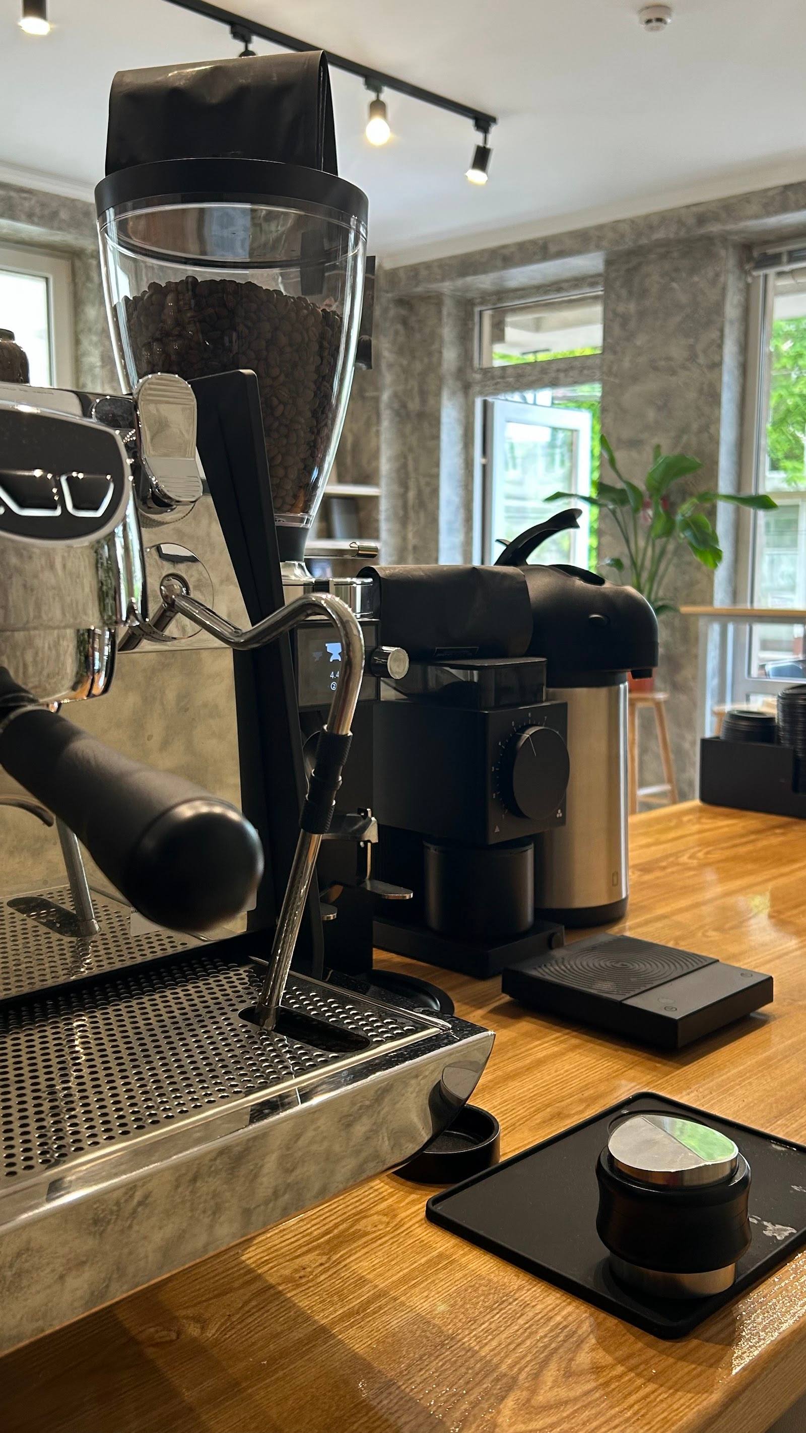 Espresso machine and grinder in modern coffee shop interior with wooden floors and large windows