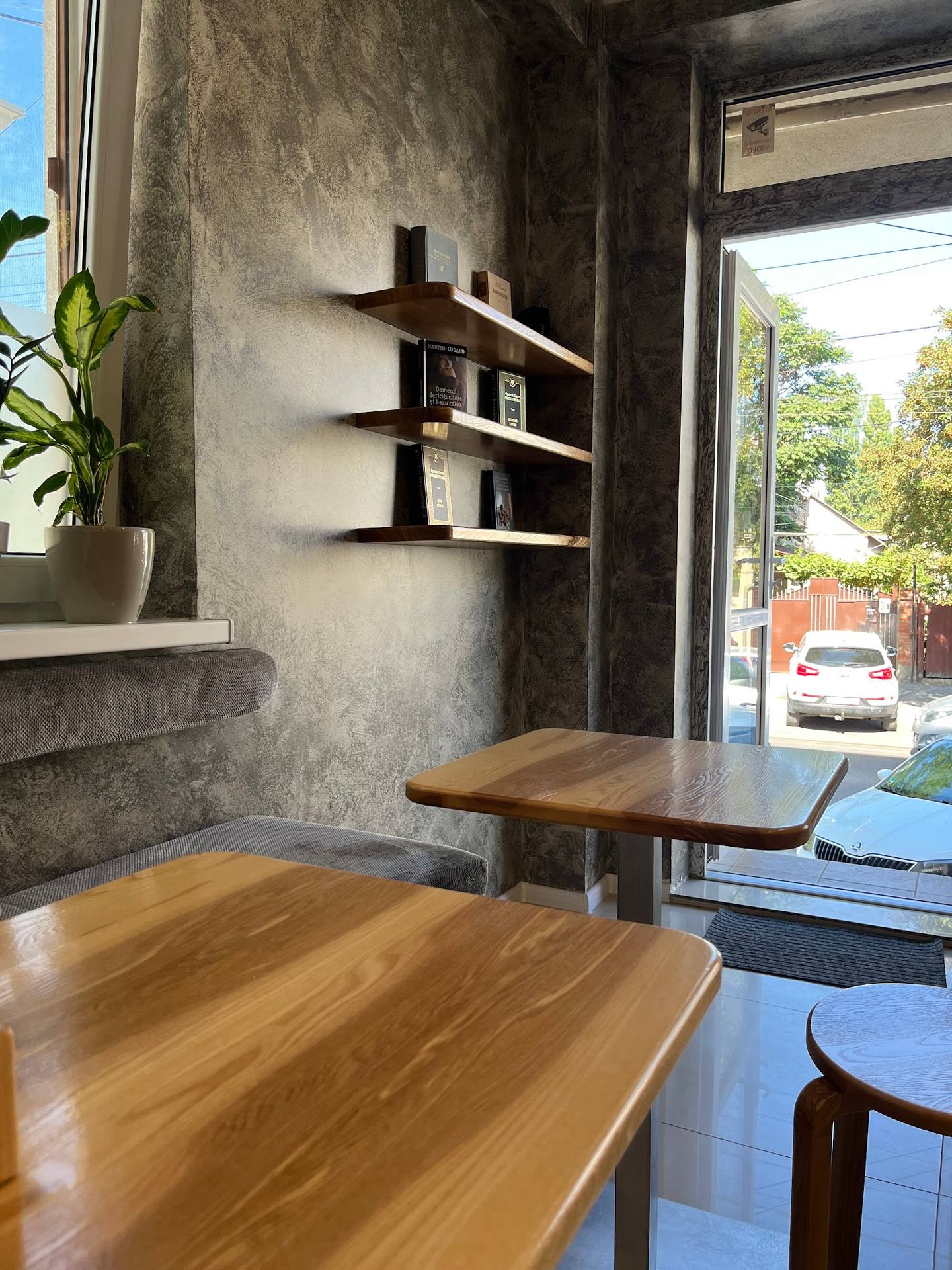 Modern café interior with wooden tables, concrete walls, and street-facing storefront view