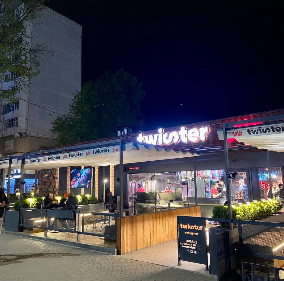 Twister bar storefront at night with illuminated signage and outdoor seating