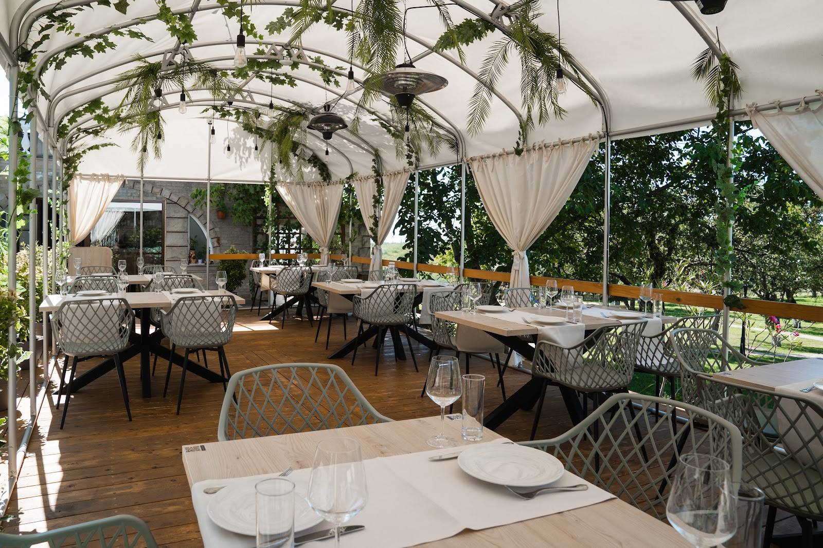 Elegant outdoor terrace with white pergola, climbing ivy, and dining tables set for service