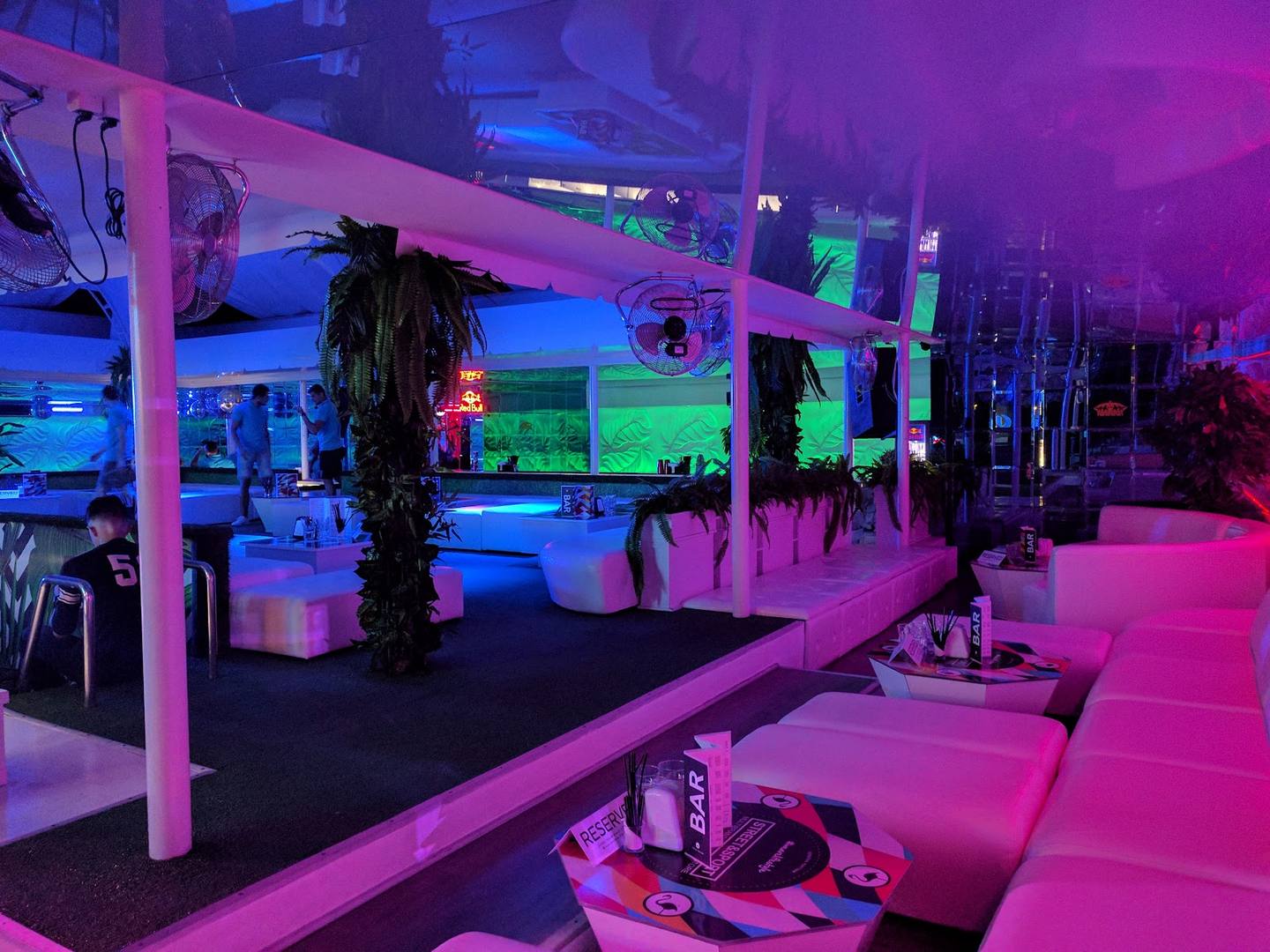 Modern nightclub interior with neon pink and blue lighting, gaming stations, and lounge seating