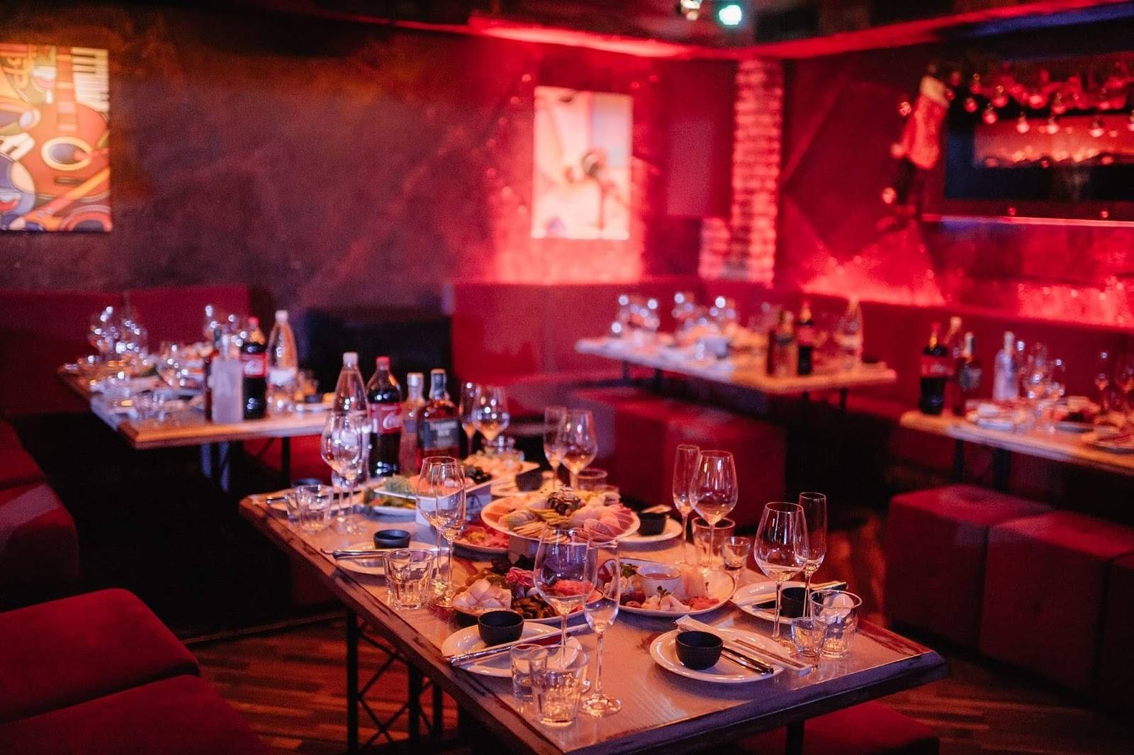 Elegant reception space with red ambient lighting, long tables, and bar counter backdrop
