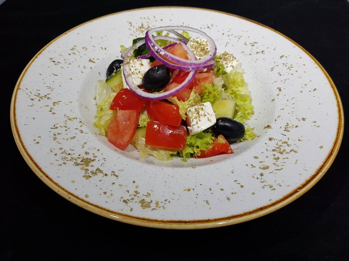 Plated Greek salad with feta, olives, tomato, and red onion on white ceramic