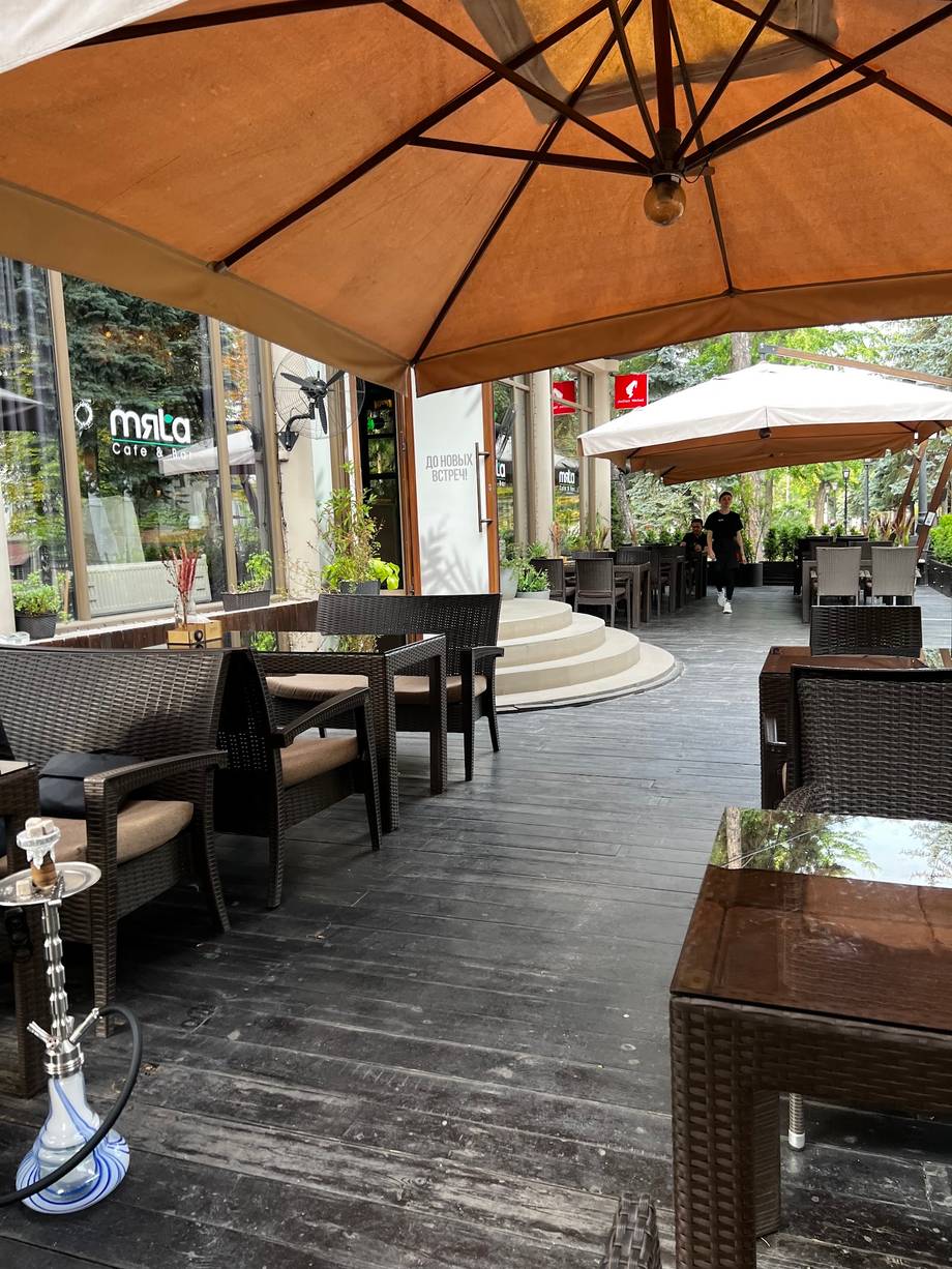Shaded terrace seating with woven umbrellas and black rattan furniture at a Moldova cafe.