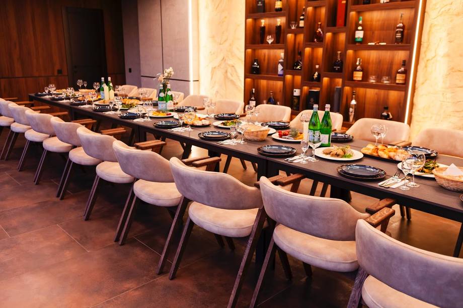 Long dining table with violet chairs and wine bottle display wall in elegant event space