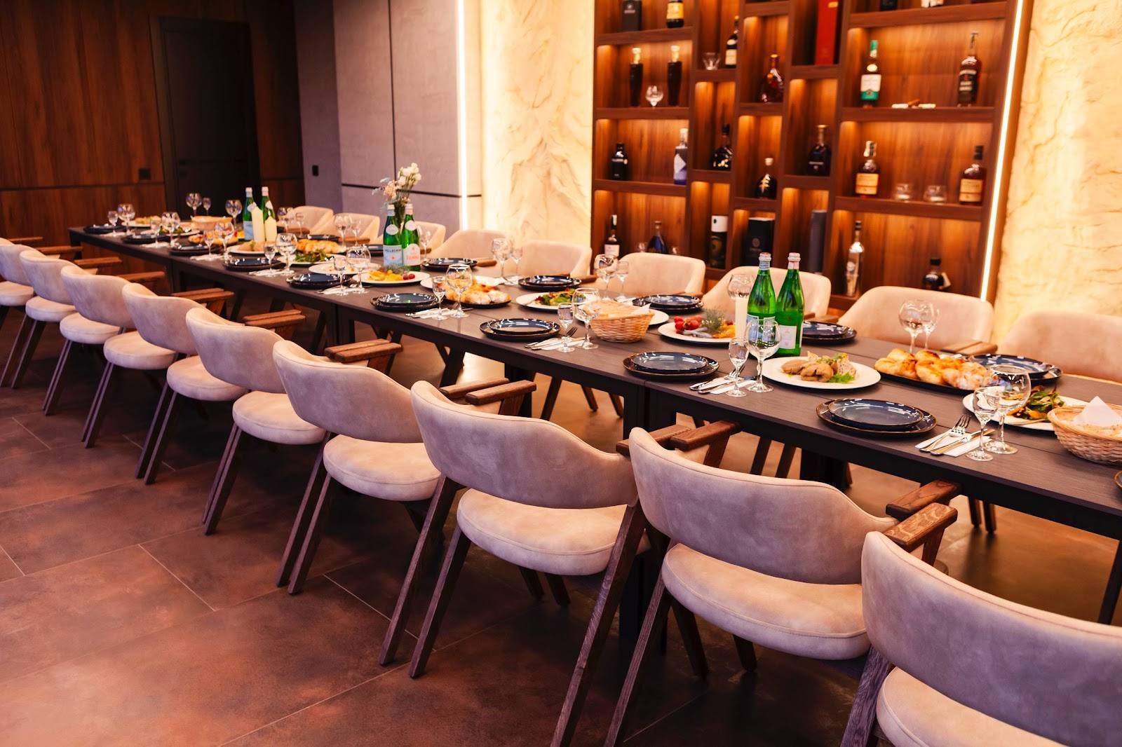Long dining table with violet chairs and wine bottle display wall in elegant event space