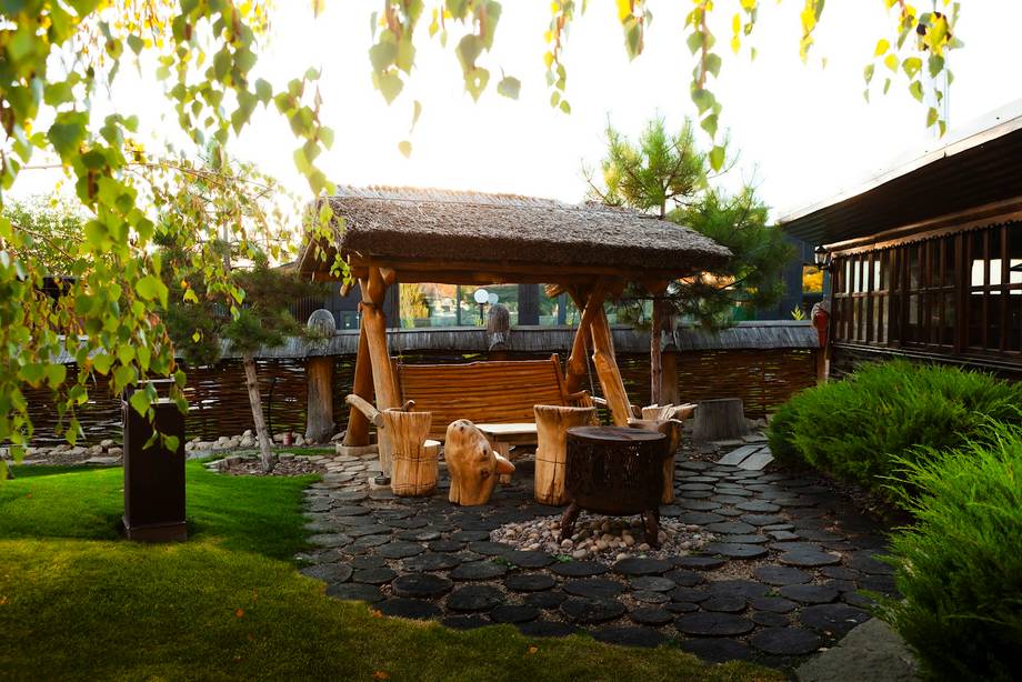 Rustic outdoor terrace with thatched-roof bar and wooden seating in a garden setting
