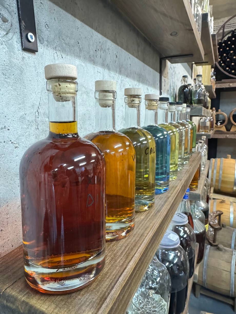 Row of craft spirits and liqueurs displayed on wooden shelf with white brick wall background