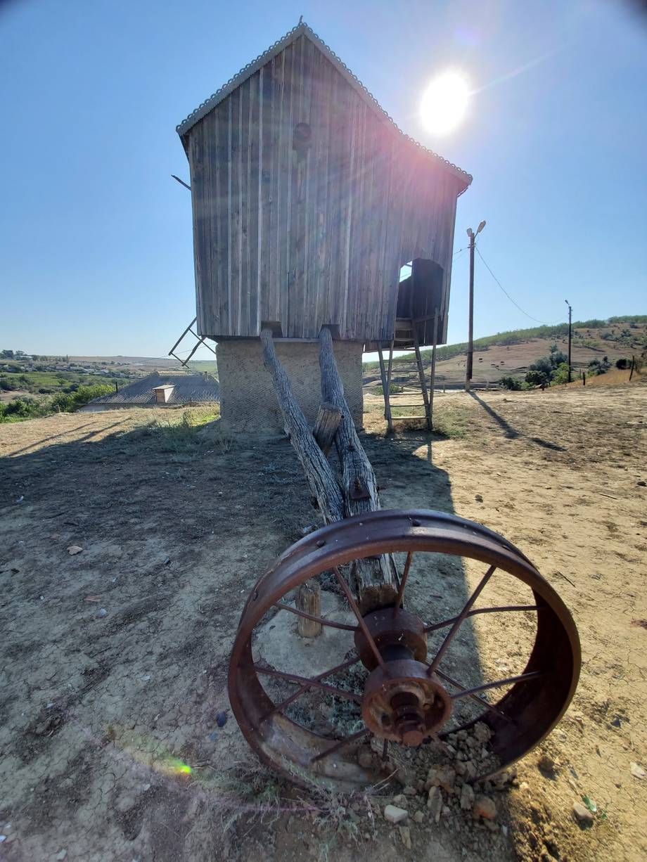 Historic wooden grain storage structure with rustic iron wheel in rural Moldova landscape