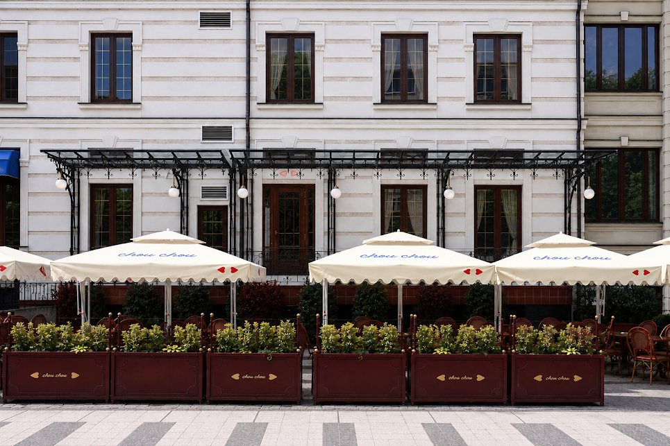 Elegant terrace facade with white umbrellas and burgundy planters on pedestrian street