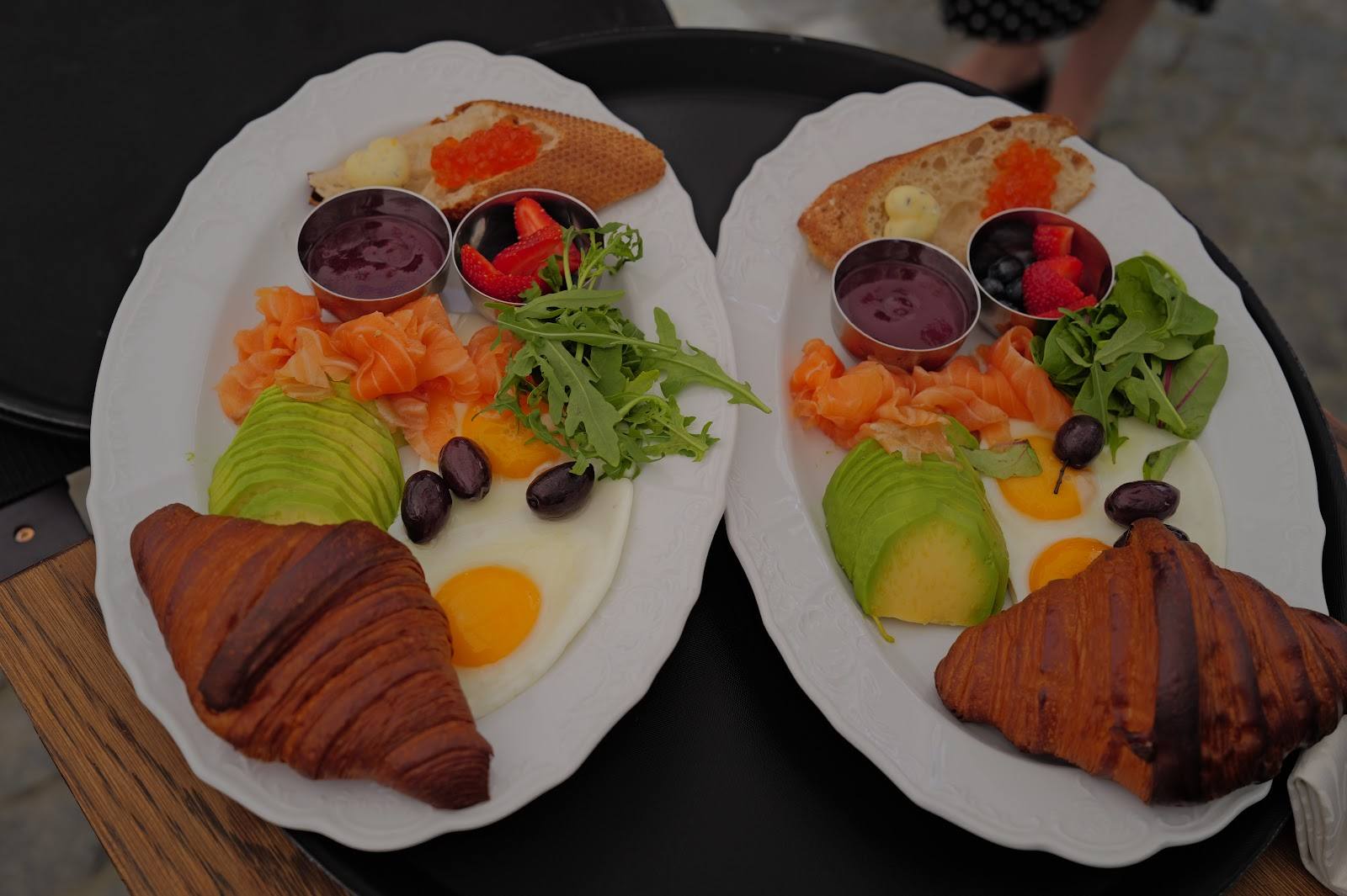 Two charcuterie and breakfast boards with cured meats, cheese, fresh fruit and croissants