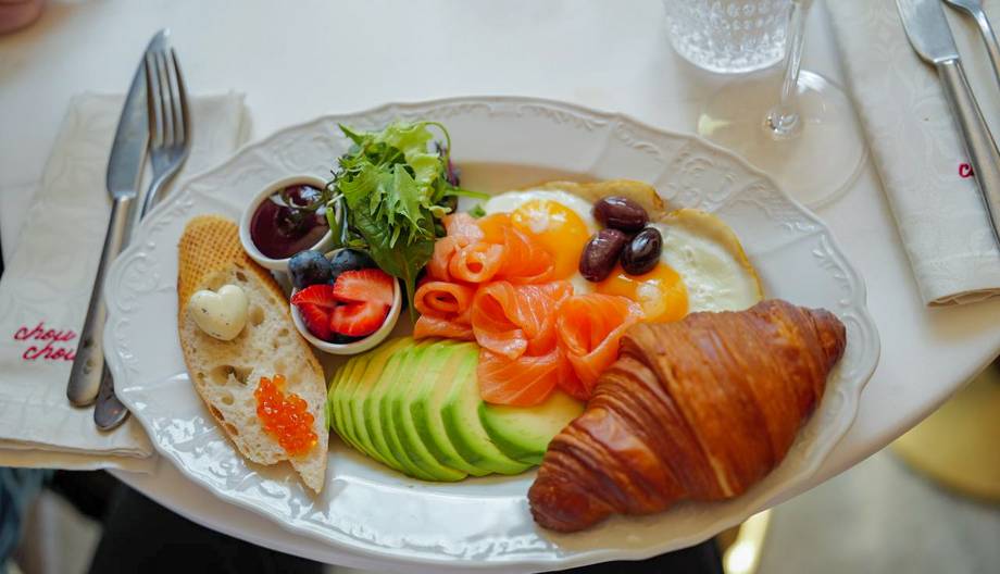 Plated breakfast with croissant, vegetables, and salmon on white oval dish