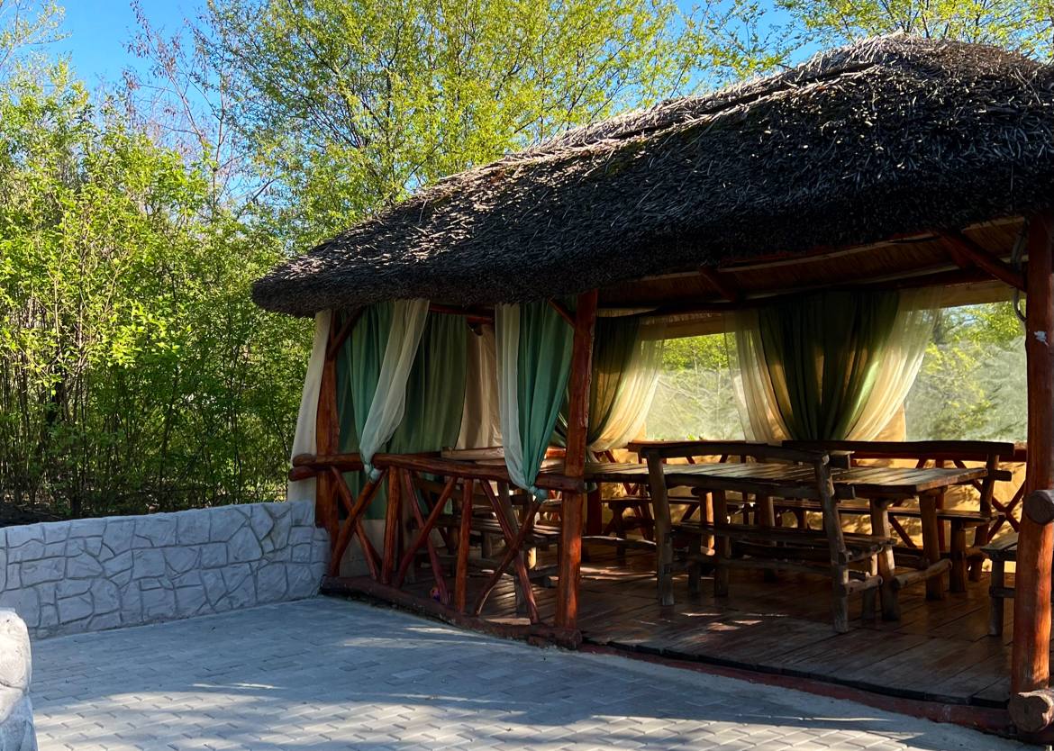 Covered wooden terrace with green curtains and rustic seating area overlooking gardens