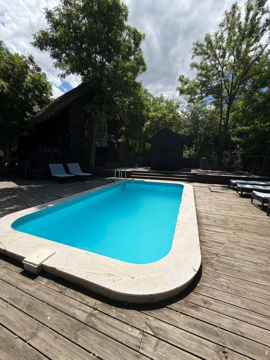 Modern resort pool with wooden deck, loungers, and lush garden setting
