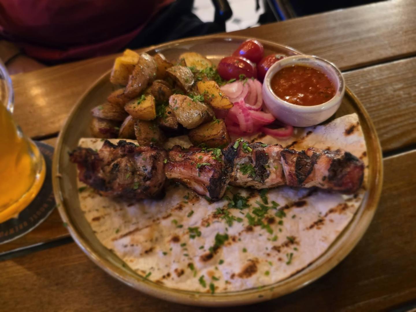 Mixed grill platter with skewers, roasted potatoes, and sauce on wooden table