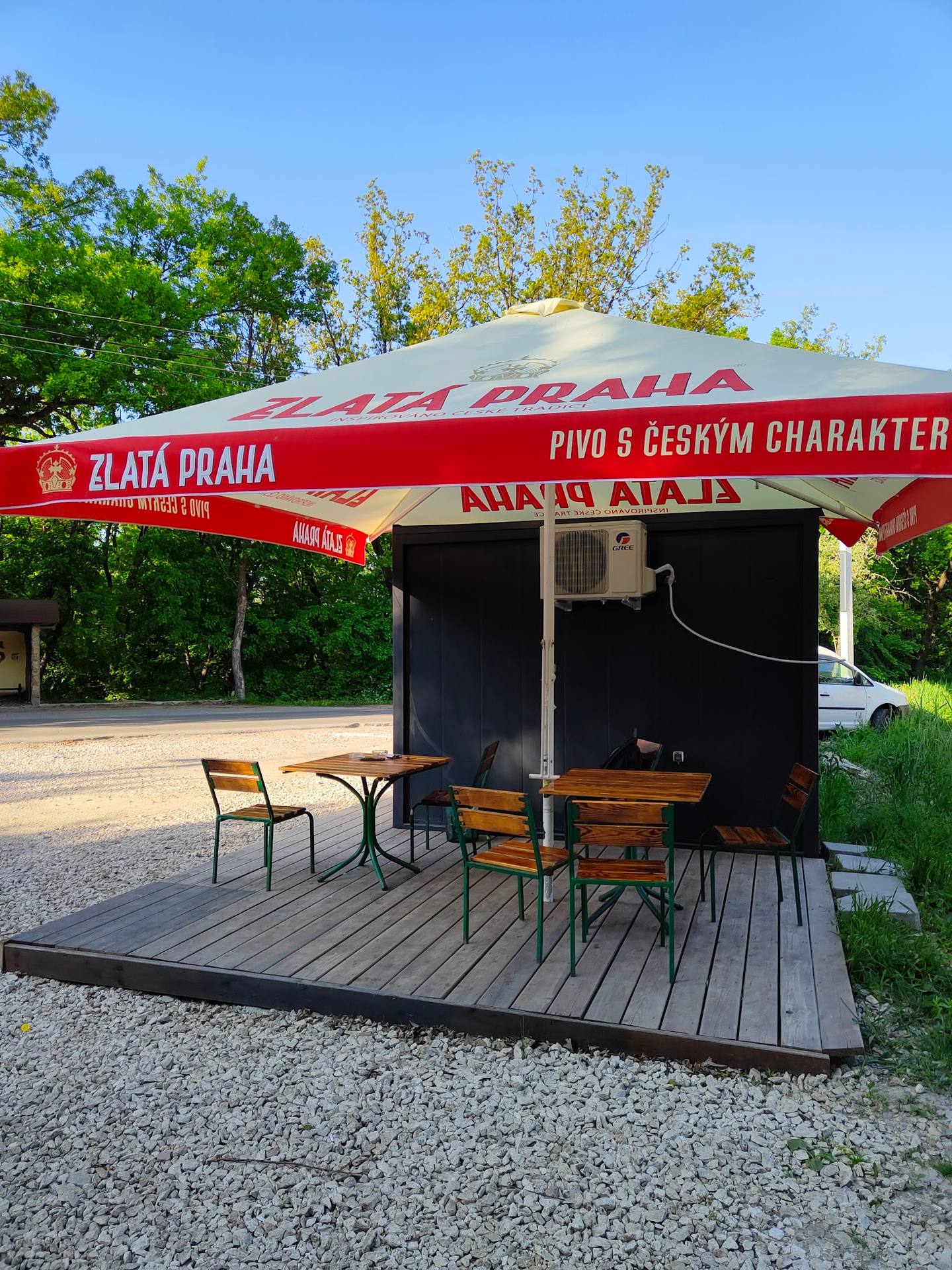 Outdoor terrace with red Zlatá Praha beer umbrella and bar counter at Czech pub venue