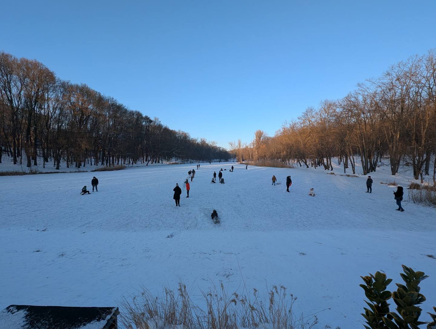 Frozen lake with winter activities and tree-lined shores under clear blue sky