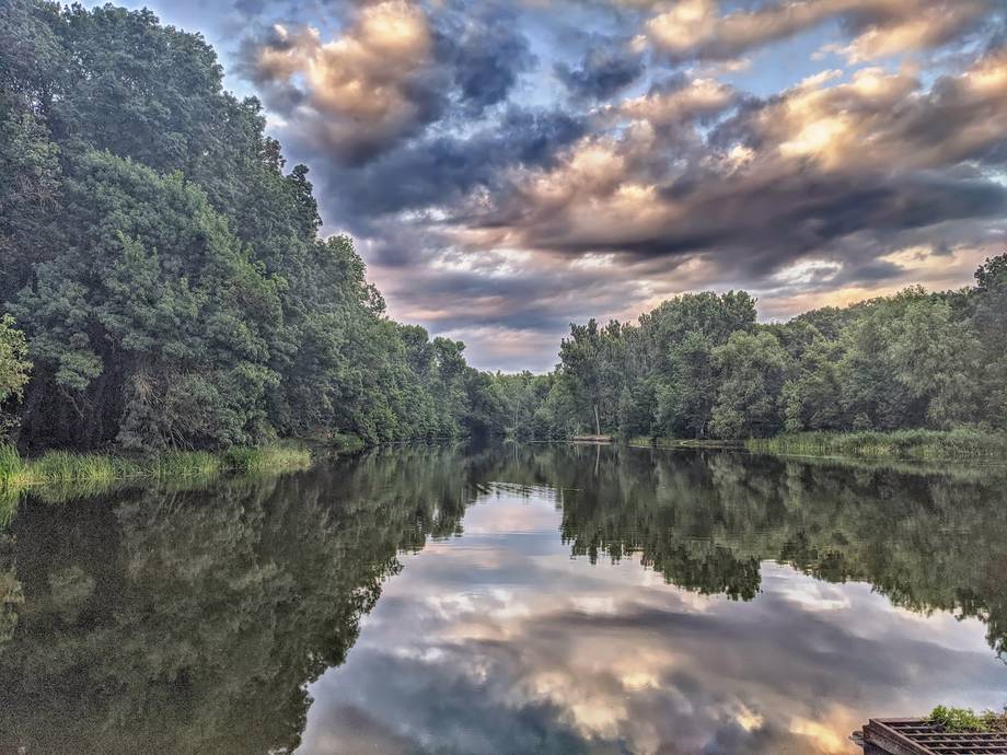 Tranquil river landscape with dramatic cloud reflections and tree-lined banks