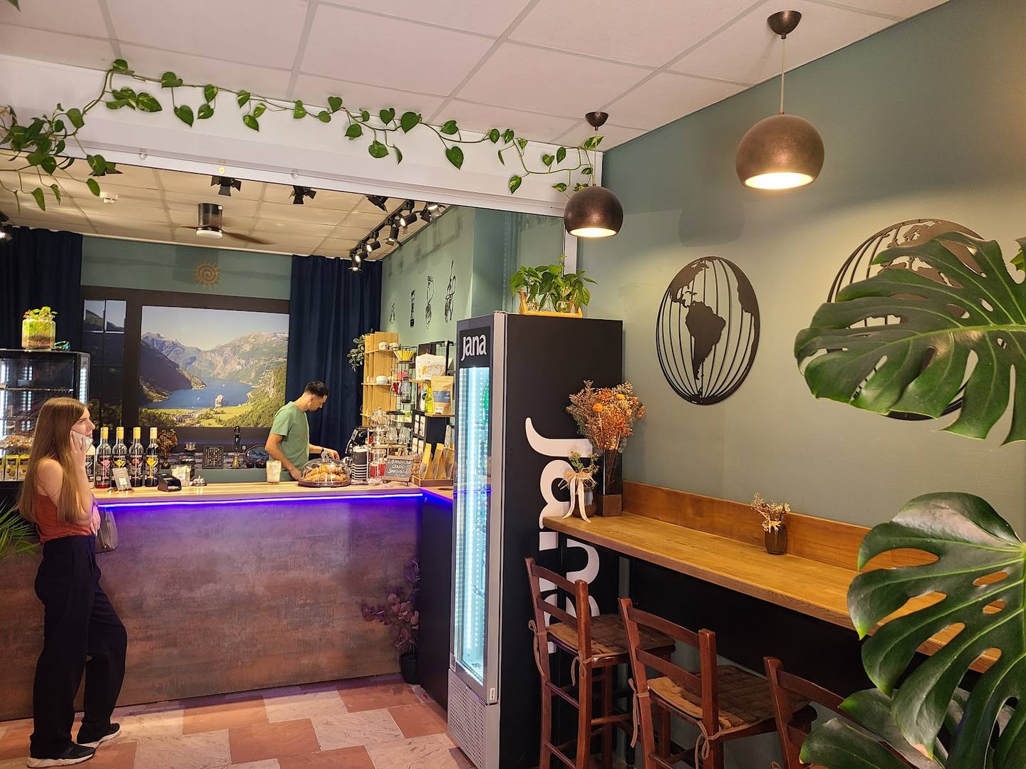 Modern café interior with purple-lit bar counter, botanical decor, and communal wooden seating