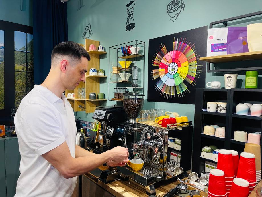 Barista preparing espresso at specialty coffee bar with branded equipment and merchandise wall
