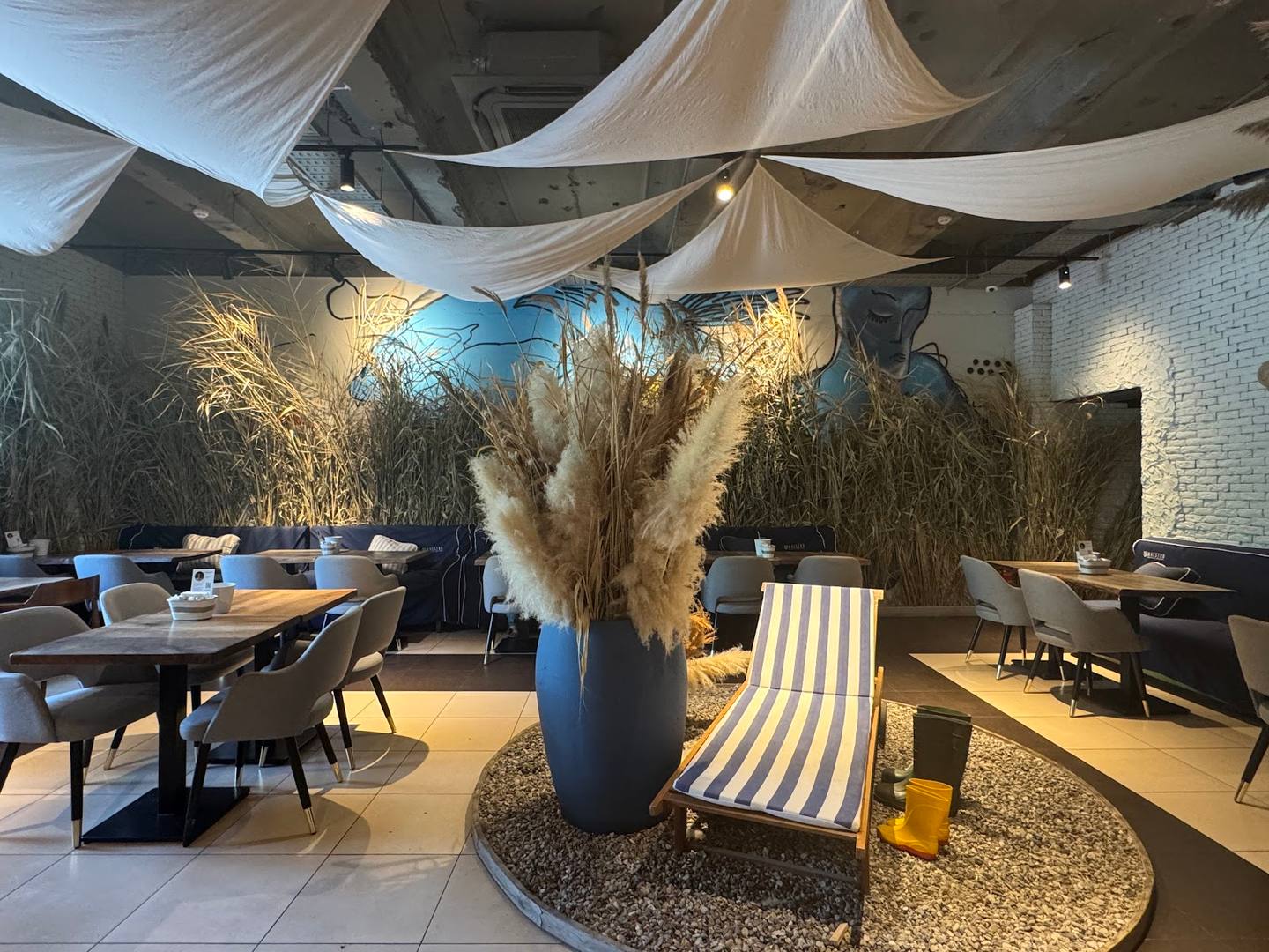 Modern restaurant interior with draped fabric ceiling, pampas grass decor, and dining tables