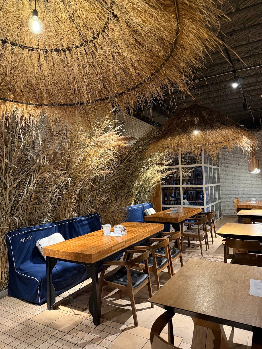 Modern restaurant interior with hanging dried grass installation and blue velvet seating