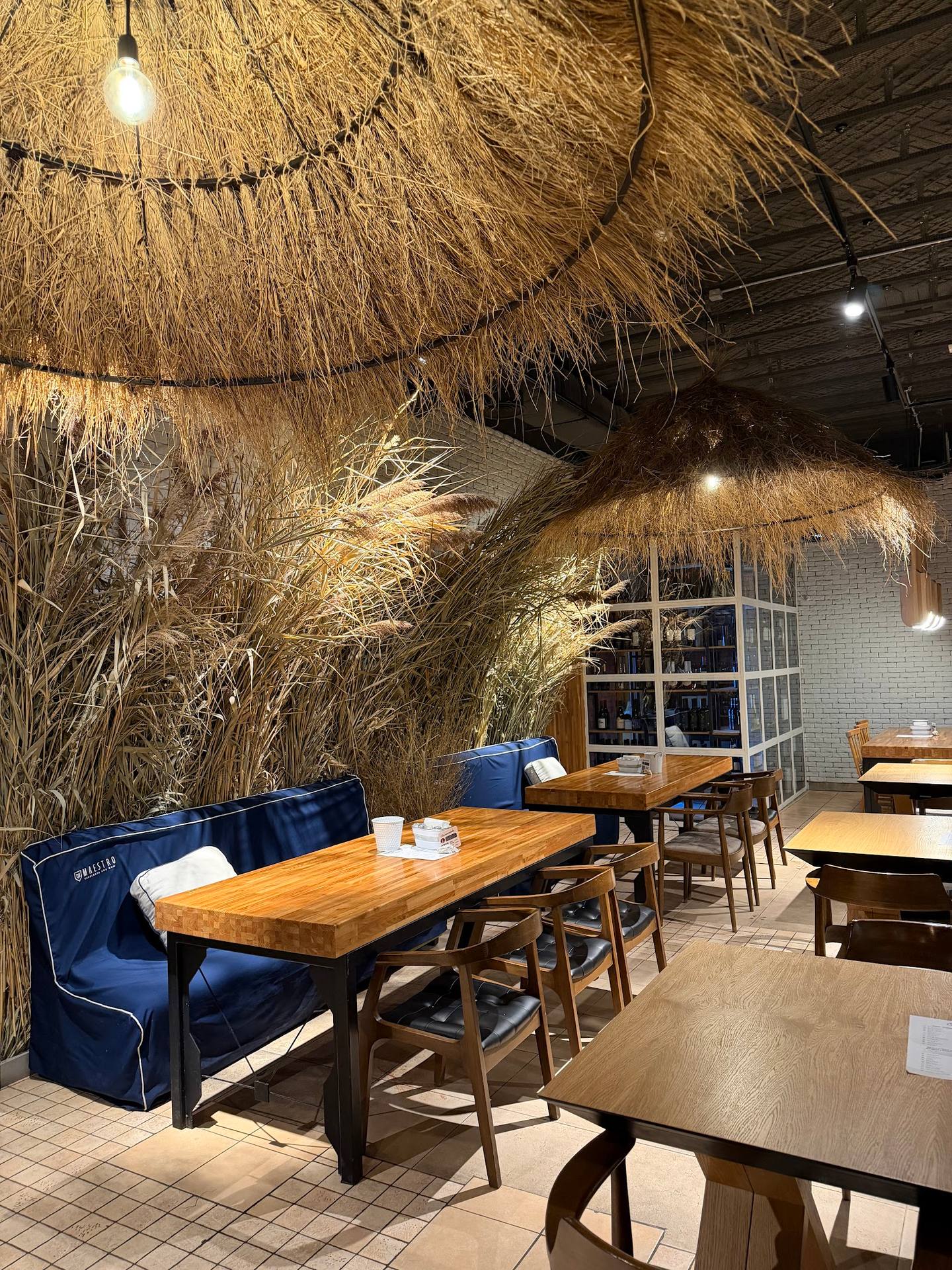Modern restaurant interior with hanging dried grass installation and blue velvet seating