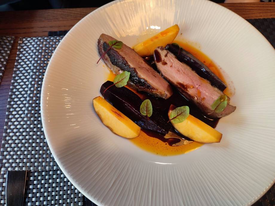 Duck breast with roasted vegetables on textured white plate