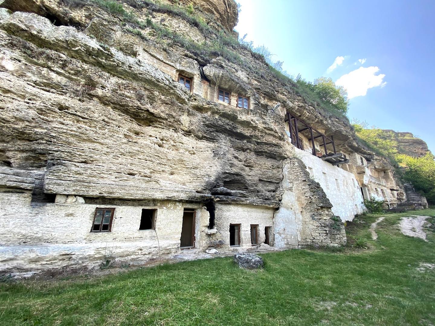 Historic rock monastery built into limestone cliff with white-washed facade and natural stone dwelling